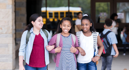 Three female students walking arm-in-arm sharing time together 